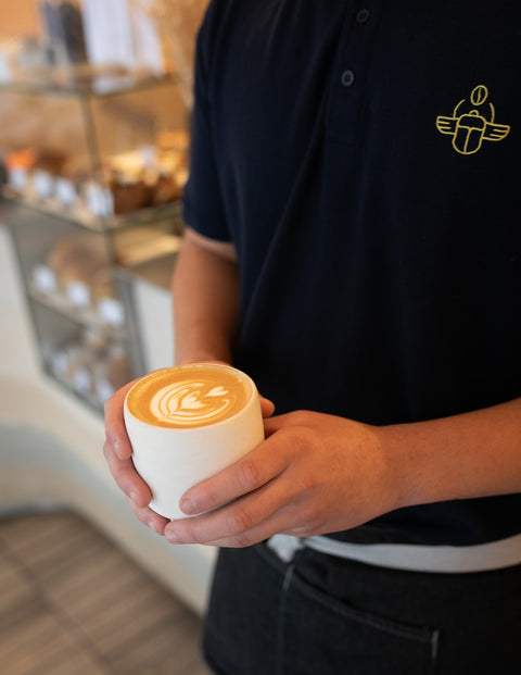 a barista holding a cup of coffee with latte art.