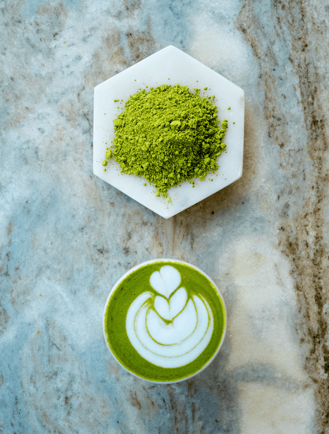 Matcha powder on a white plate next to a cup of matcha latte with latte art